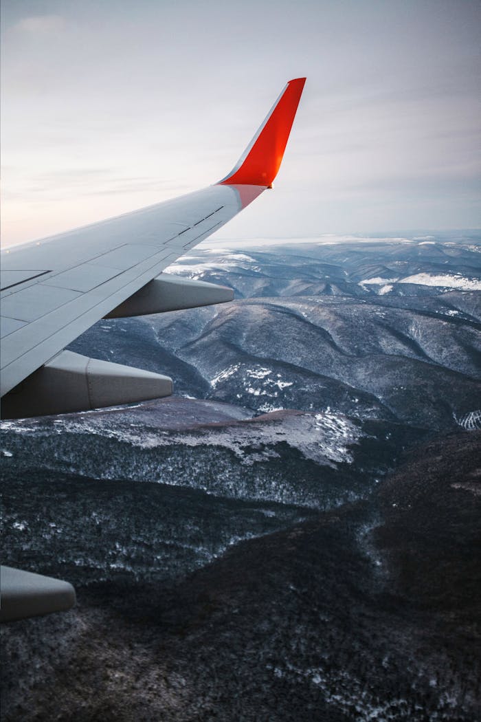 Scenic aerial view of a mountain range covered in snow, seen from an airplane wing.